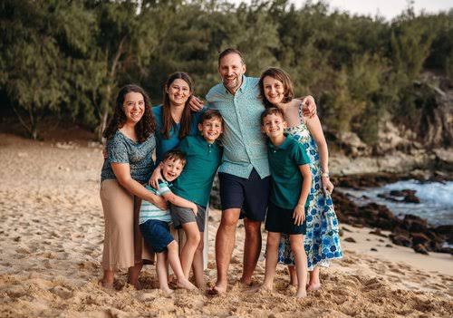 Family standing together beside trees and a rocky beach