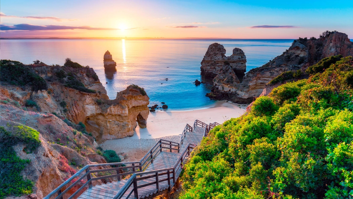 Wooden stairs leading toward a rocky coastal beach at sunset